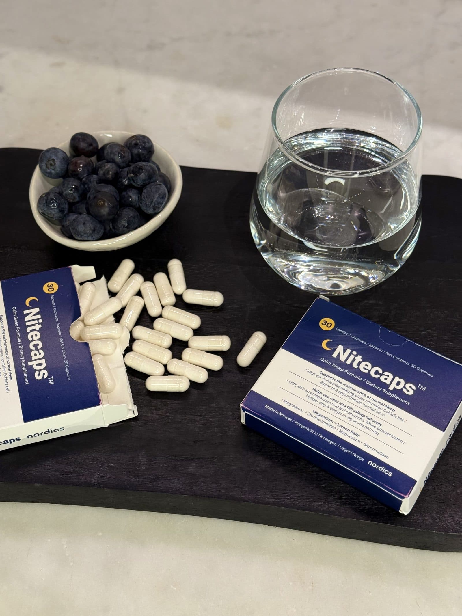 NiteCaps melatoninevrij voedingssupplement met capsules en een glas water.